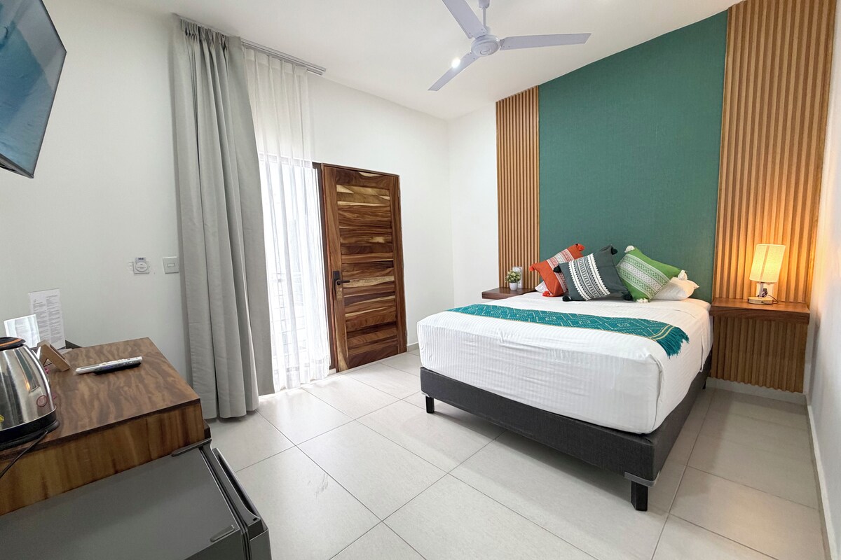 A hotel room with a bed, a desk, a television, a ceiling fan, and a window with curtains.