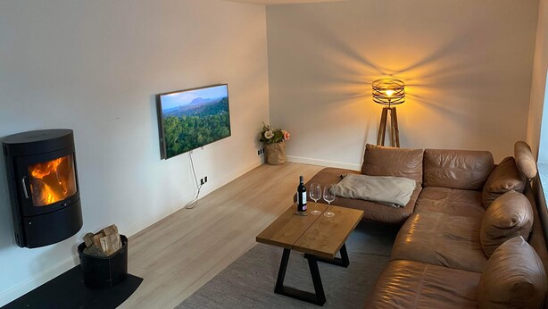 Ein Wohnzimmer mit Kamin, Flachbildfernseher, Couchtisch aus Holz, Sofa und Stehlampe.