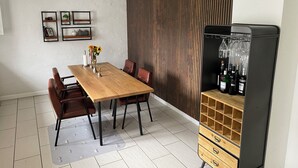 Ein Essbereich mit einem Holztisch und Stühlen, einem schwarzen Kühlschrank mit Weinflaschen und einer Wand mit vertikalen Hol zleisten.