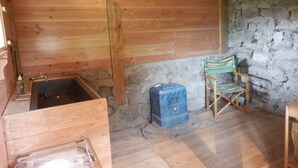 A rustic wooden cabin interior with a stone wall, a wooden bench, and a small wooden table.