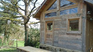 A rustic wooden cabin with a stone foundation, large windows, and a picnic table in front.
