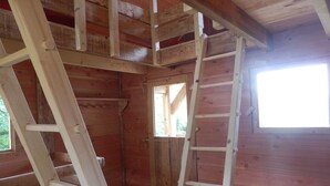 A wooden cabin interior with a wooden ladder and a window.