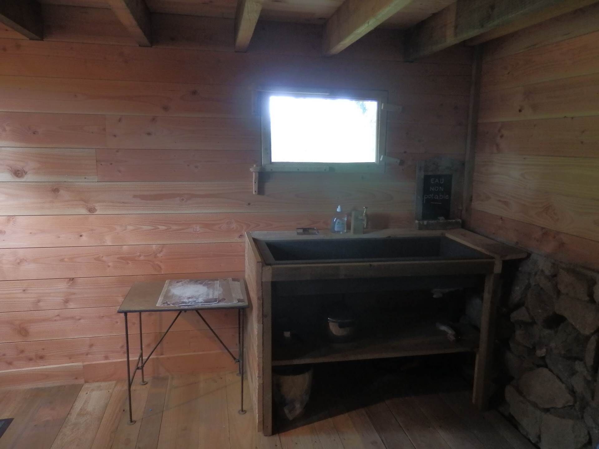 Ein Holzblockhaus-Interieur mit einem Holzbecken, einem kleinen Hocker und einem Fenster.