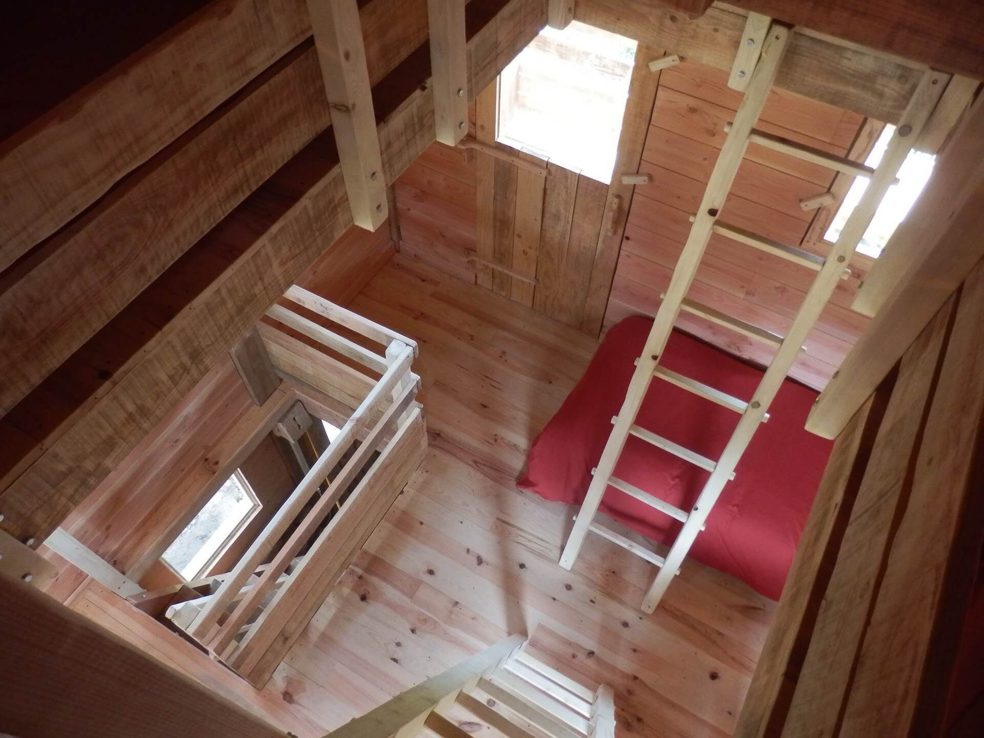 Eine Holzhütte mit Schlafkoje, rotem Kissen und einer Leiter.