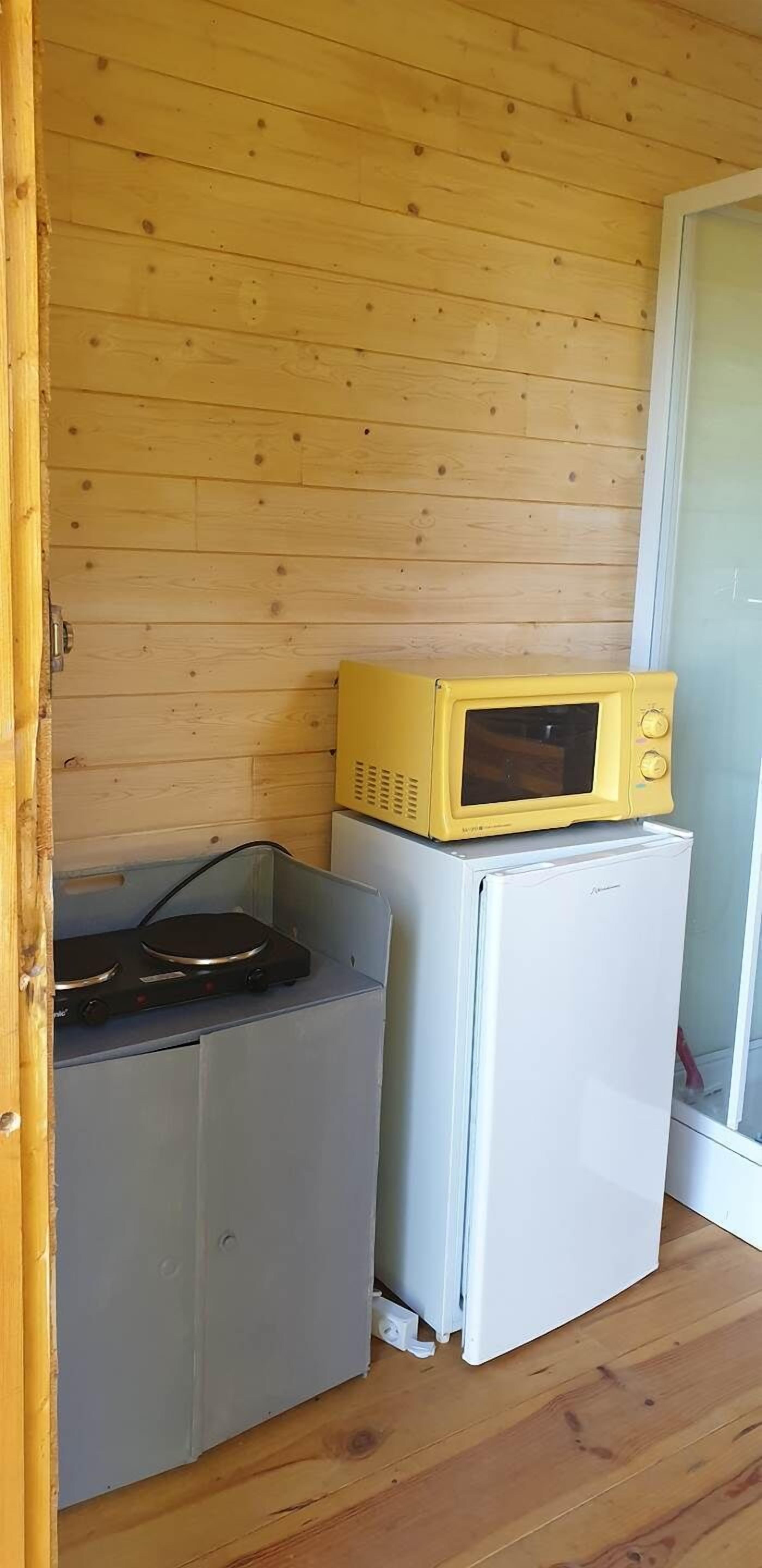 Een compacte kitchenette met een magnetron boven een kleine koelkast, een fornuis en een kastje.