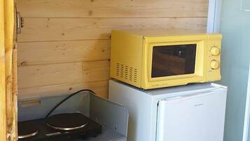 Een compacte kitchenette met een magnetron boven een kleine koelkast, een fornuis en een kastje.