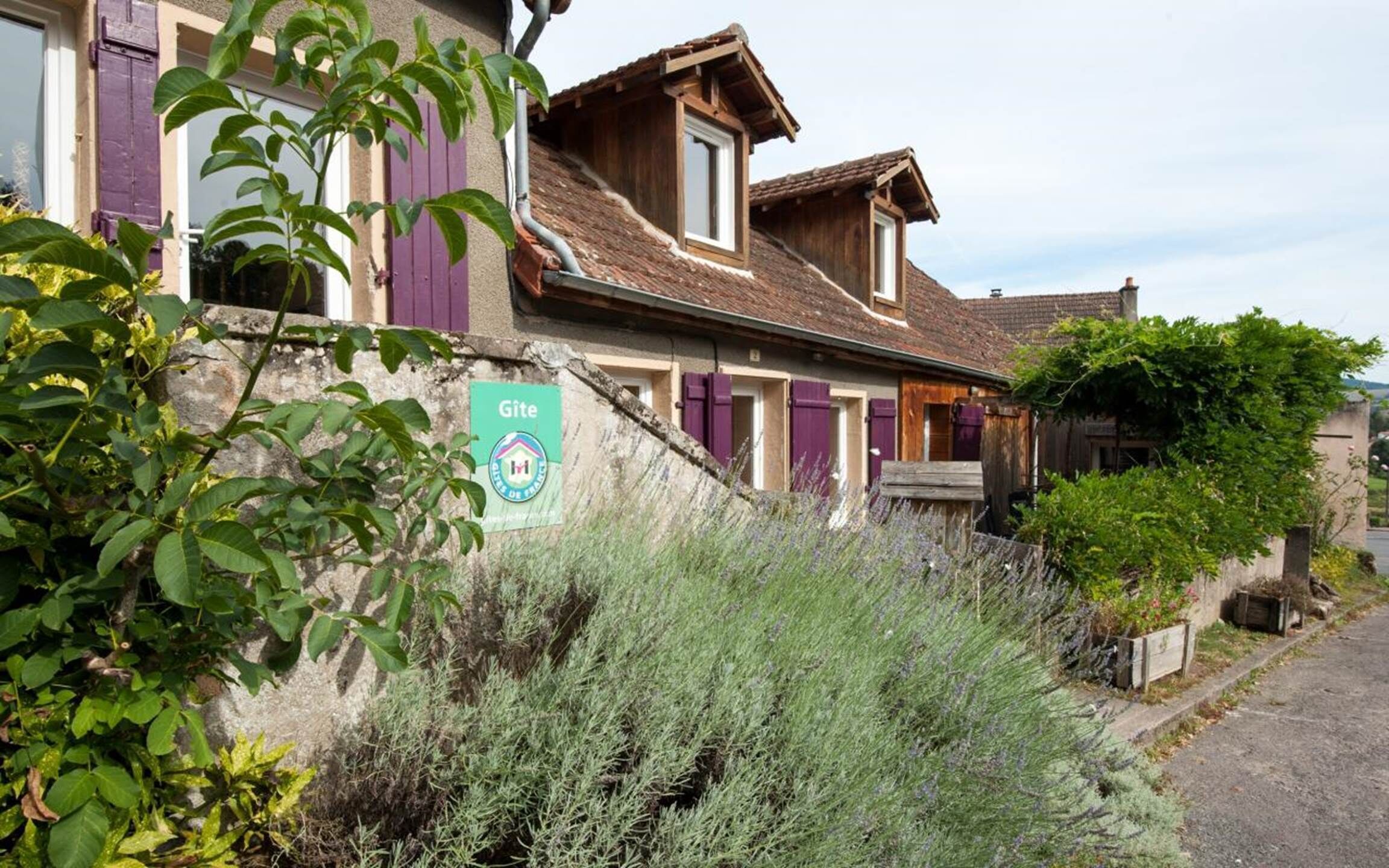 A rustic building with a stone facade, wooden shutters, and a sign indicating it is a gîte.