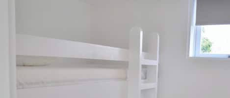 A bunk bed with a ladder, white walls, and a window.