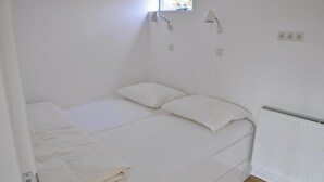 Een kleine eenpersoonskamer met witte beddengoed, een raam met uitzicht en een radiator aan de muur.