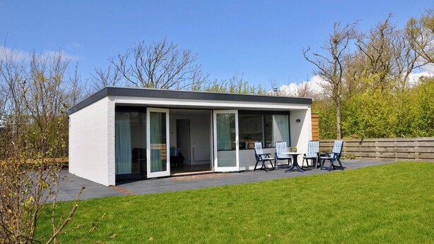 Een modern huis met een plat dak, grote schuifpuien en een terras met tuinmeubilair.