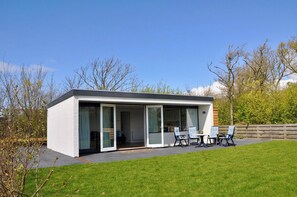 A modern house with a flat roof, large sliding glass doors, and a patio with outdoor furniture. - Bungalow in Callantsoog Near Sandy Beaches (Callantsoog)
