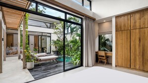A modern bedroom with a large bed, a desk, and a view of a swimming pool and greenery. - Blue Kai Villa by Alfred in Bali (Pecatu)