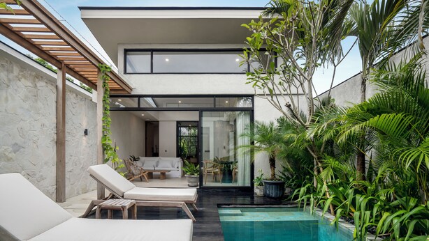A modern outdoor pool area with lounge chairs, a stone wall, and lush greenery. - Blue Kai Villa by Alfred in Bali (Pecatu)
