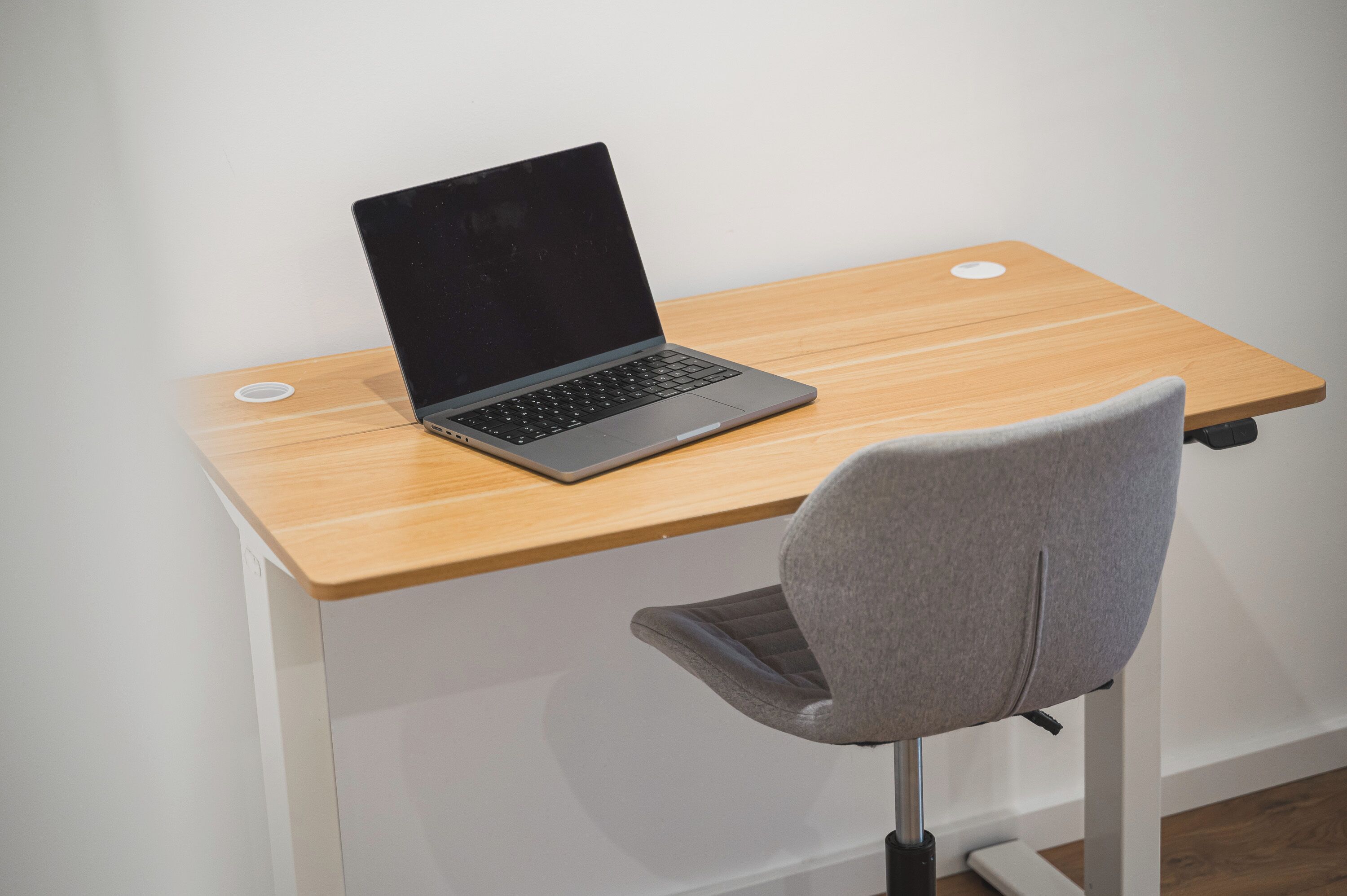 A laptop on a wooden desk with a grey chair.