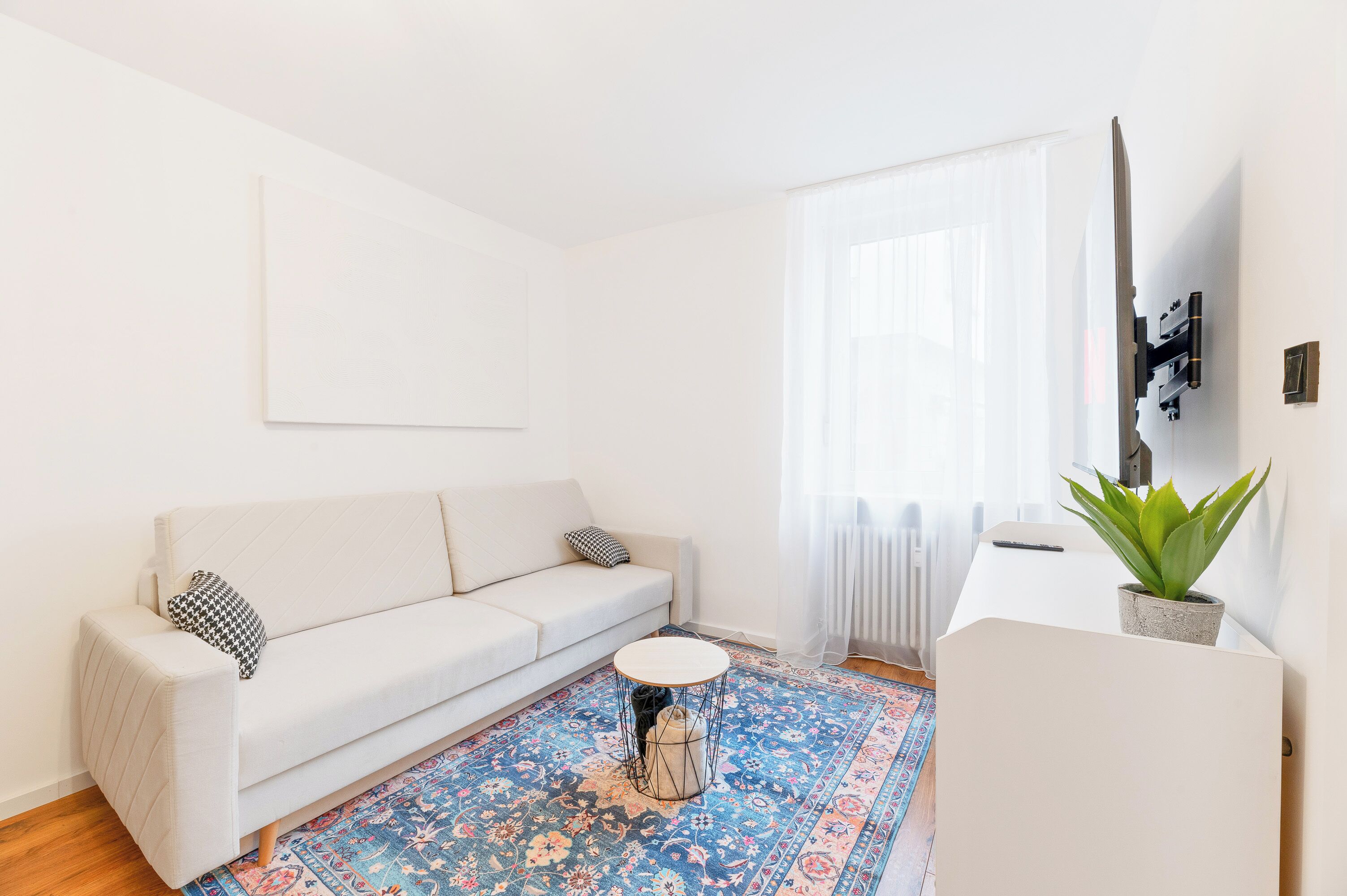 A modern living room with a white sofa, a round coffee table, and a patterned rug.