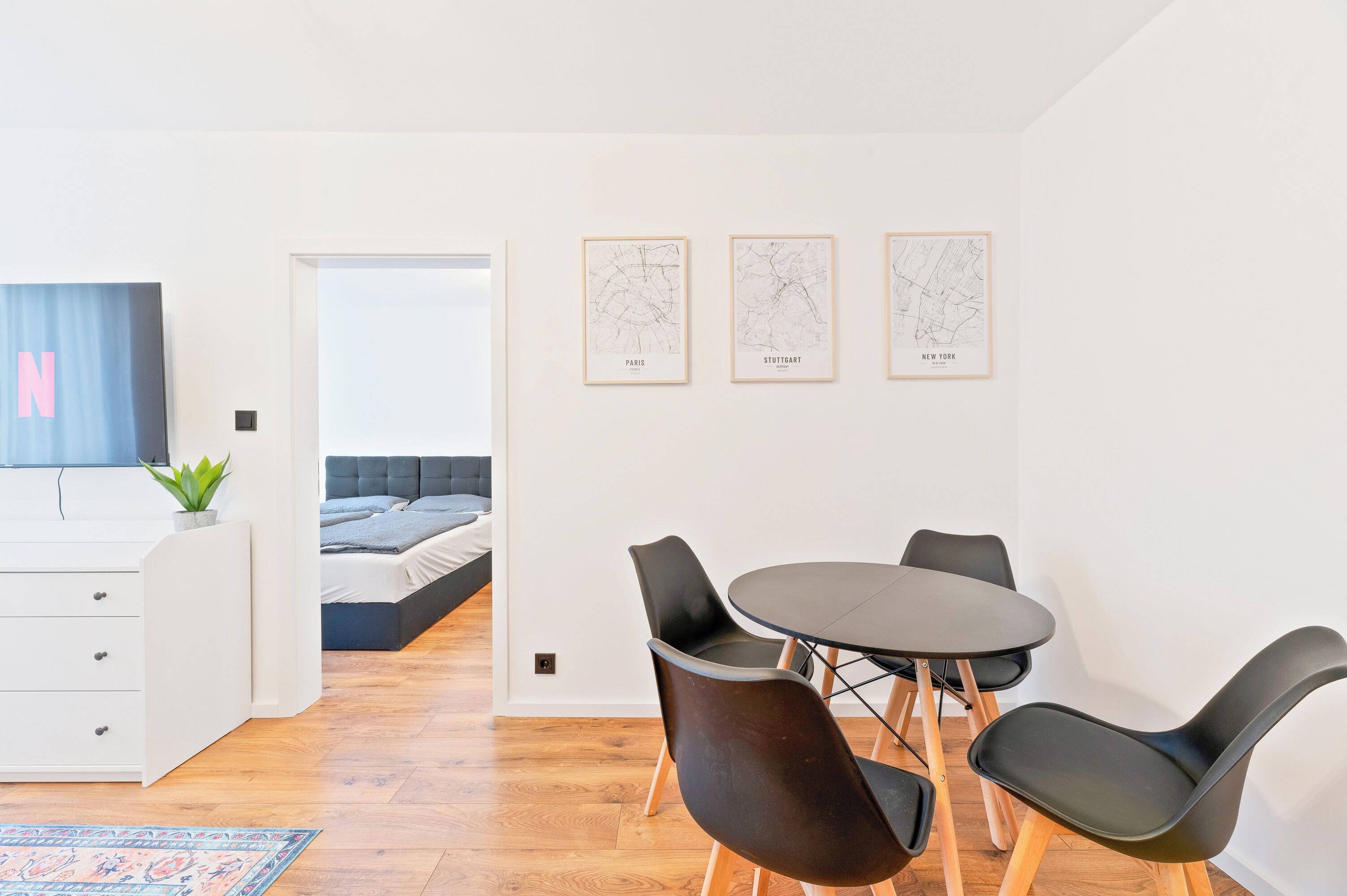A modern room with a bed, a desk, a TV, and three framed maps labeled Paris, Stuttgart, and Moscow.