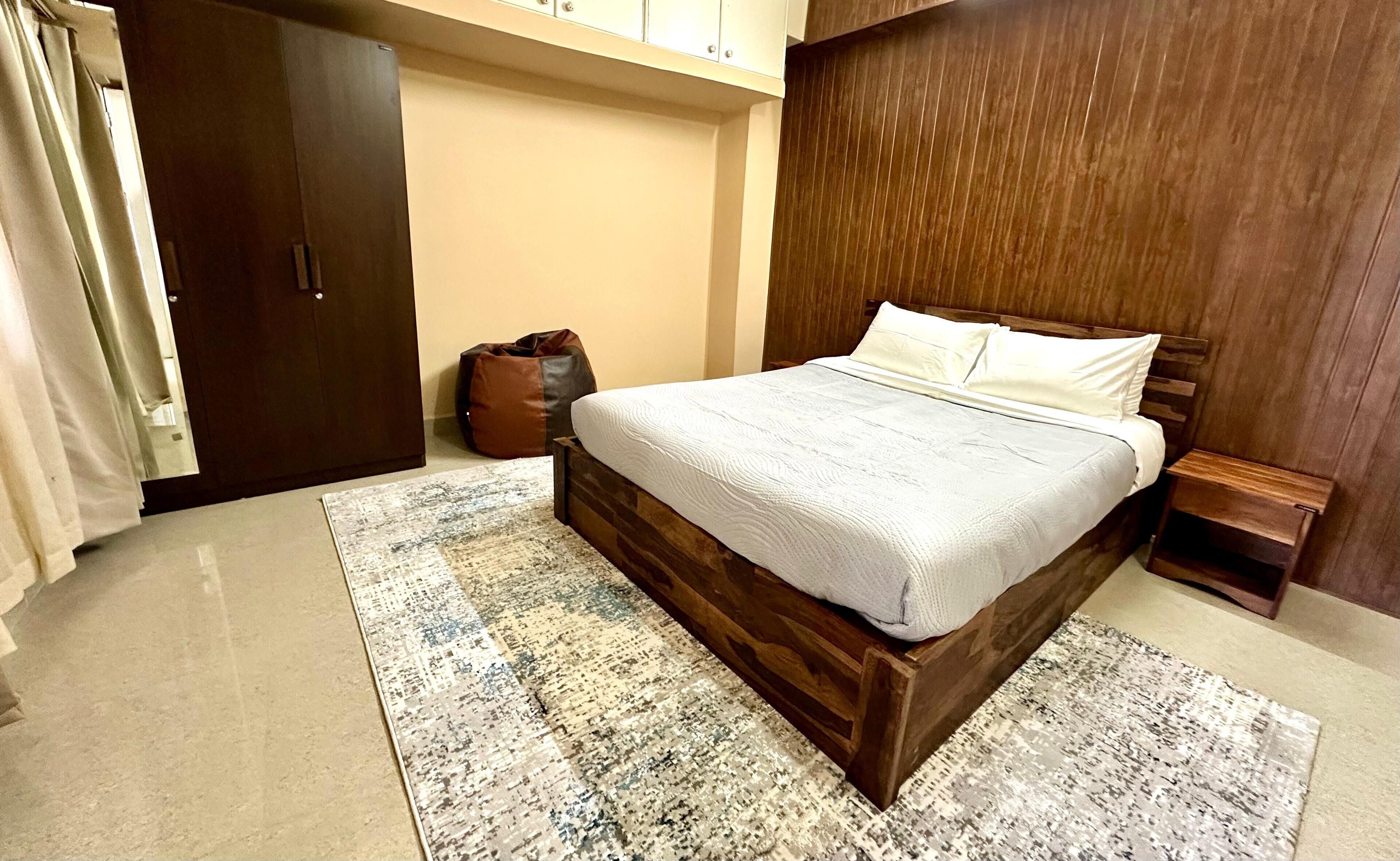Ein Schlafzimmer mit einem hölzernen Bettgestell, einem gemusterten Teppich, einer braunen Tasche und einem Holzschrank.