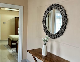 Un pasillo con un banco de madera, un jarrón blanco con flores y un espejo decorado en la pared.