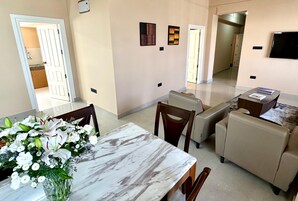 Un salón amplio con una mesa de mármol, sofás color beige y un televisor de pantalla plana montado en la pared.