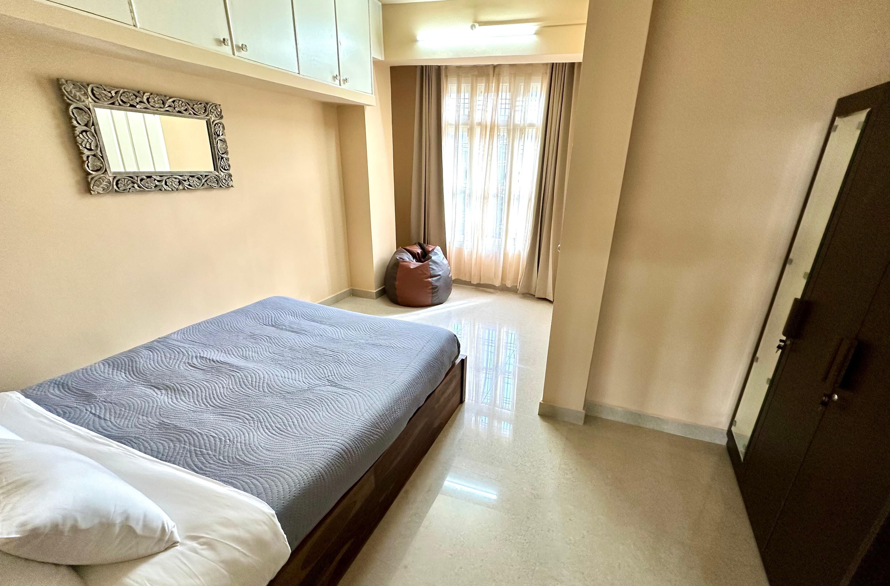 Une chambre avec un lit, un fauteuil poire, un miroir et une armoire.