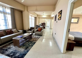 Una sala de estar moderna con un sofá, una mesa de centro y sillones. Se ve un comedor al fondo, con una mesa y sillas.
