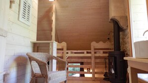 A wooden cabin interior with a fireplace, a wicker chair, and a wooden railing. - Nature-themed Bed and Breakfast (Broye)