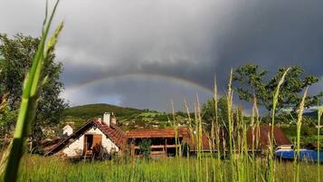 Paisagem rural com uma casa, campos e um arco-íris.
