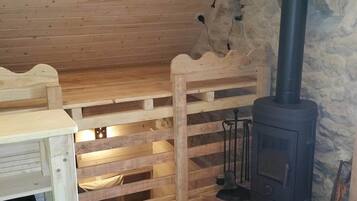 Interior acolhedor de uma cabana com um banco de madeira, lareira e uma parede rústica de pedra.