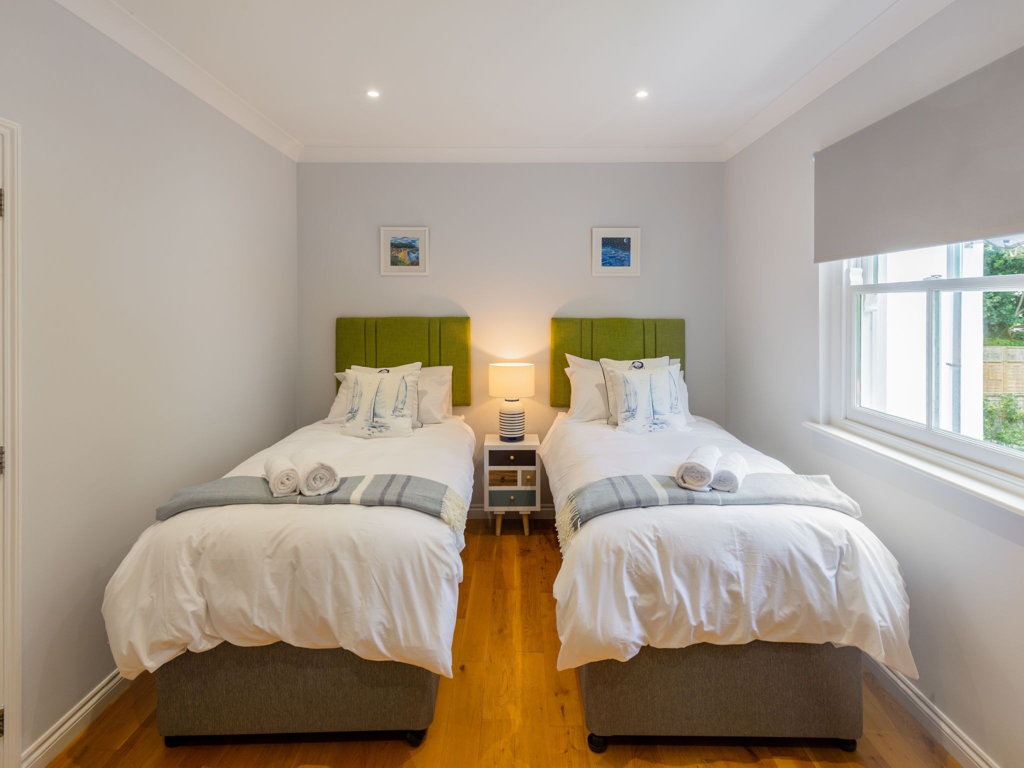 A double room with two beds, each with a green headboard, white bedding, and a small bedside table with a lamp.