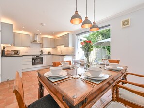 A modern kitchen with white cabinets, a built-in oven, and a dining area with a wooden table set for four. - Sea Compass by Interhome (Charlestown)
