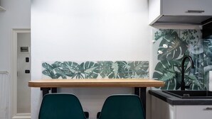 Una cocina con una mesa de madera, dos sillas verdes y un salpicadero con motivos de hojas tropicales.