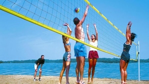 Een strandvolleybalwedstrijd met spelers in zwemkleding, een net en een zandstrand met water op de achtergrond.