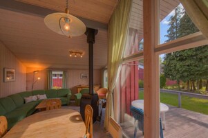 Ein gemütliches Blockhauss Innenleben mit einem Holzesstisch, einem grünen Sofa und einem großen Fenster mit Blick auf einen Garten.