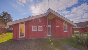 Een rood gebouw met een schuin dak, een voordeur en twee ramen.
