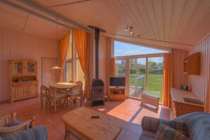 Una habitación acogedora con detalles de madera, chimenea, televisión y un amplio ventanal con vistas al exterior.
