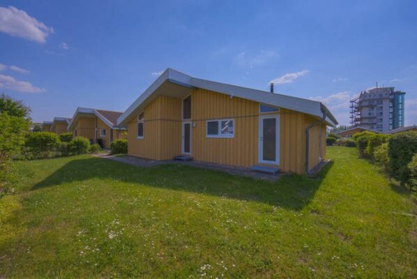 Una hilera de casas modernas de madera amarilla con techo plano, rodeadas de césped verde y un cielo azul despejado.