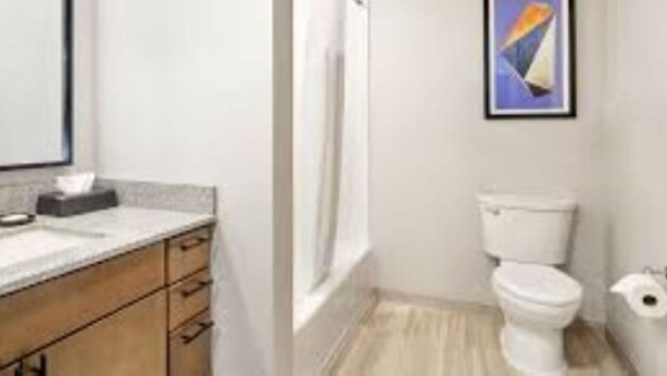 Une salle de bain avec un lavabo blanc, des meubles en bois, des toilettes blanches et une douche.