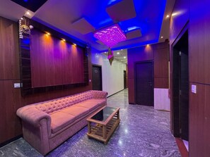 A modern lobby with a pink sofa, a glass coffee table, and a ceiling with blue lighting.