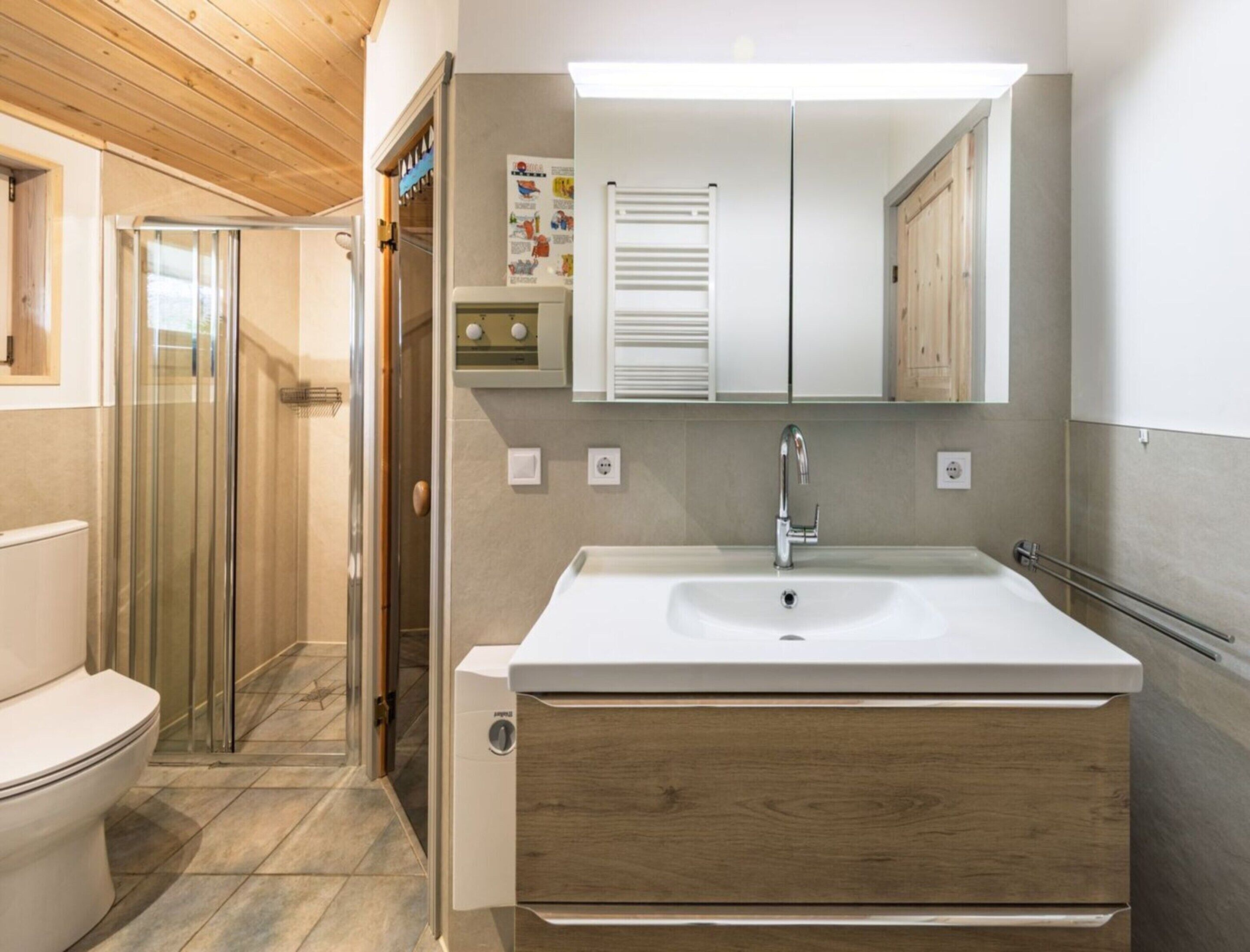 A modern bathroom with a large sink, wooden cabinet, and a glass shower enclosure.