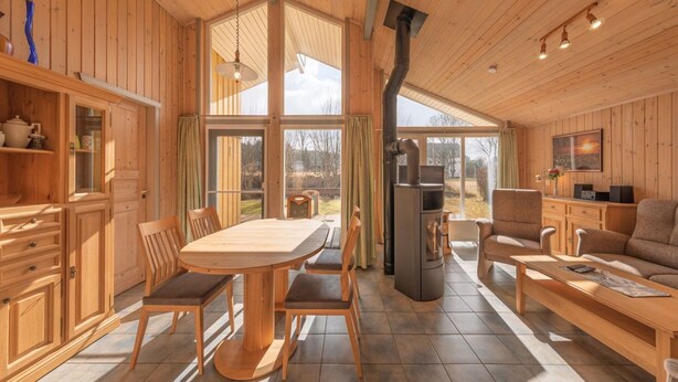 A wooden cabin interior with a dining table, chairs, a sofa, and a fireplace. - Ferienhaus mit Sauna im Ferienpark Mirow (Mirow)