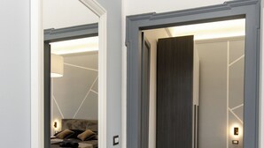 A hallway with a large mirror, a dark door, and a glimpse of a bedroom with a bed and a nightstand. - VivimiHome-Navigli Exclusive Apartment (Milan)