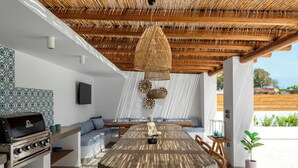 Un espace de restauration en plein air avec une table ronde, des chaises en bois, un barbecue et un luminaire suspendu.