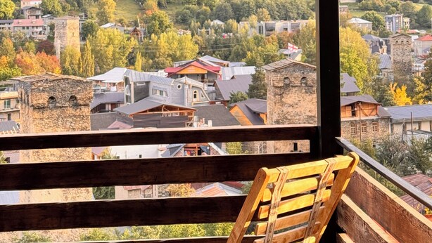 Un balcone in legno con vista su un pendio boscoso e un villaggio sottostante.