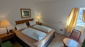 A hotel room with a double bed, two bedside lamps, a framed picture on the wall, a chair, and a window with curtains. - Gasthof Hotel Rose (Eisenheim)
