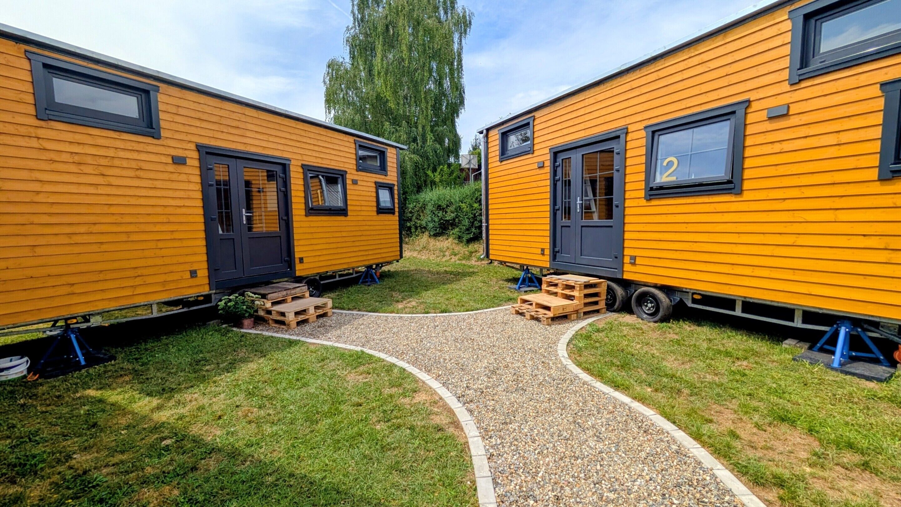 Two yellow mobile homes with black doors and windows, connected by a gravel path.