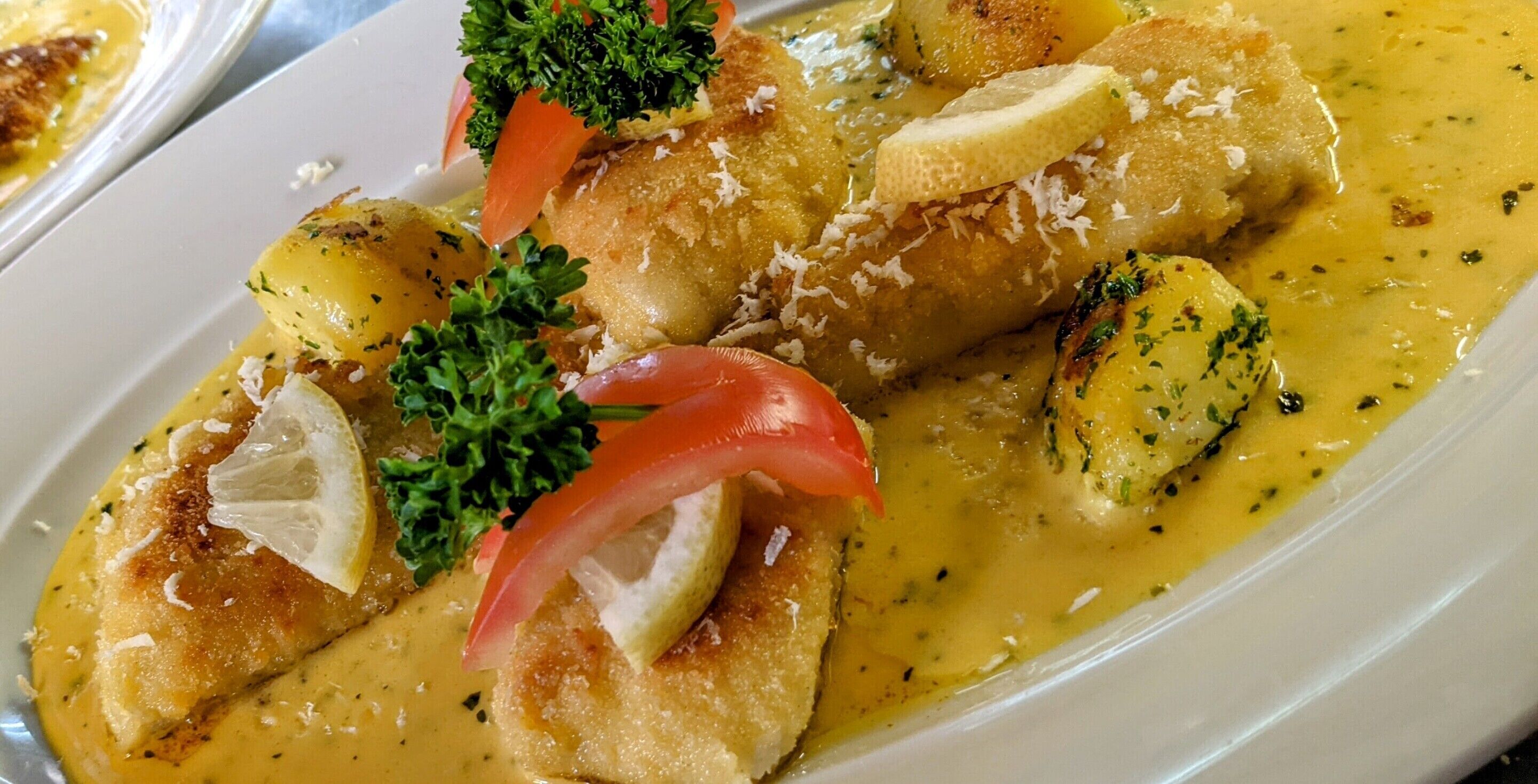 Un plato de comida con pescado, patatas y guarniciones.