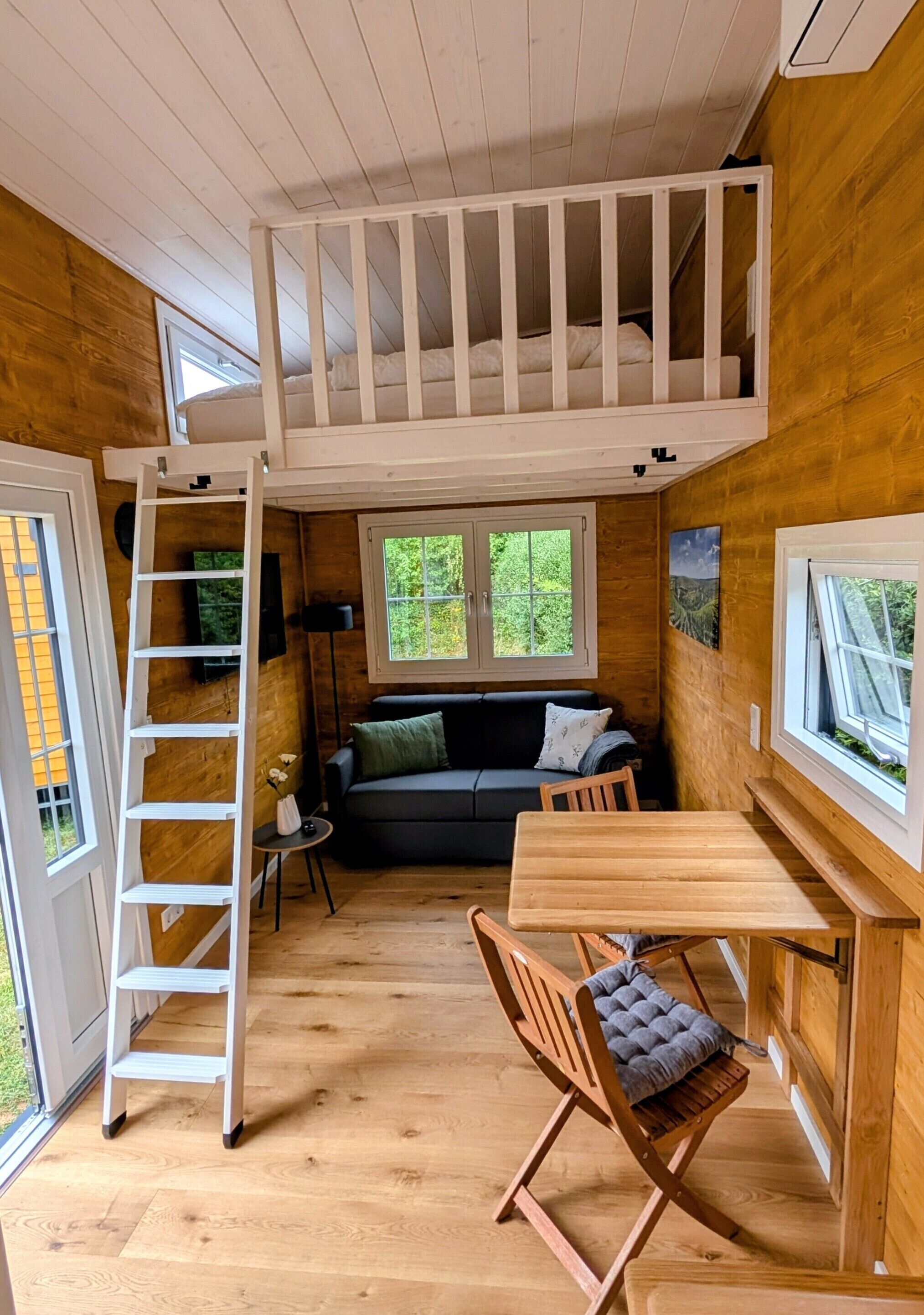Quarto estilo loft com beliche, mesa de madeira, cadeira, mesinha lateral e sofá.