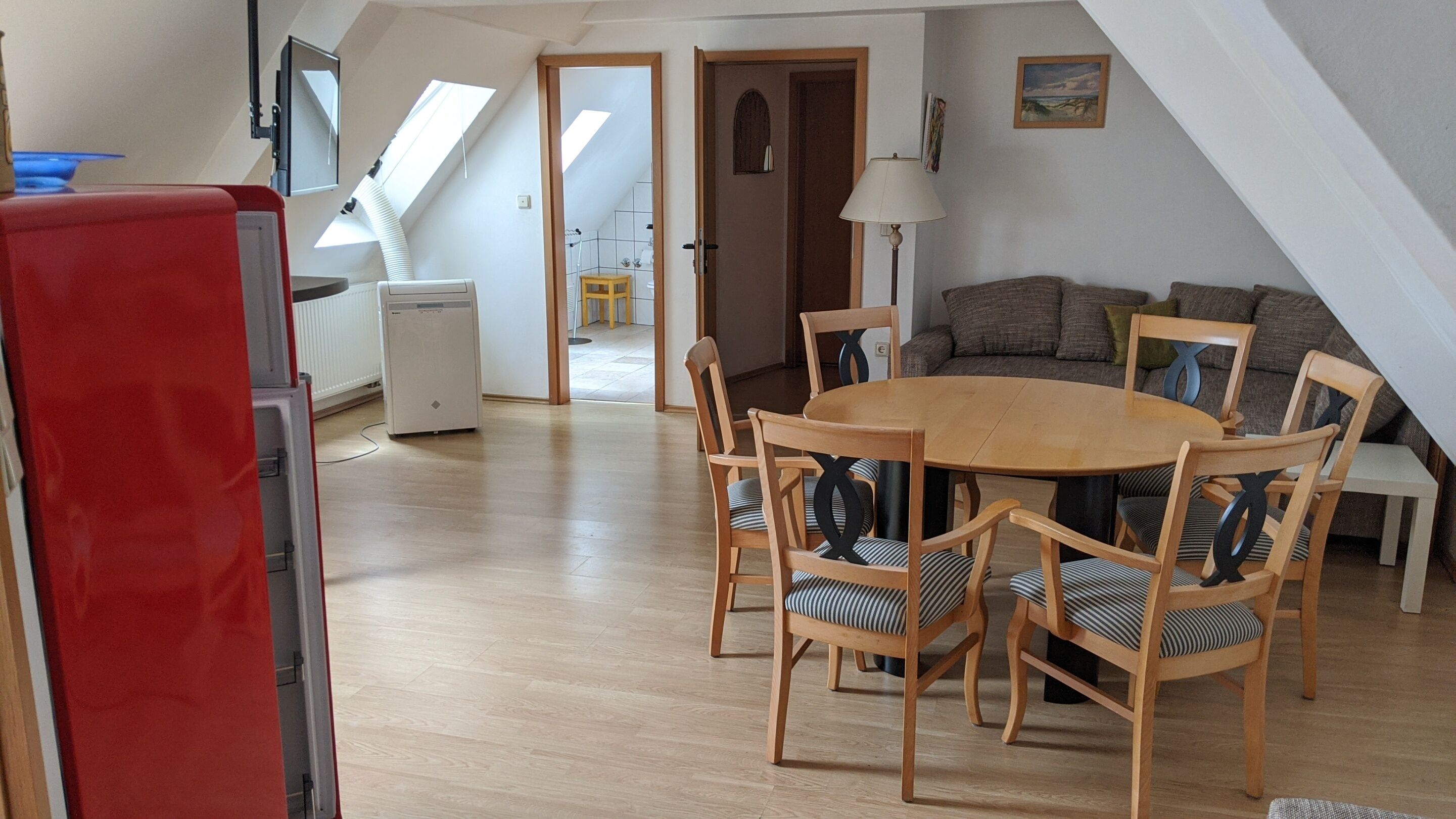 A spacious living area with a round wooden table and chairs, a sofa, and a red refrigerator.