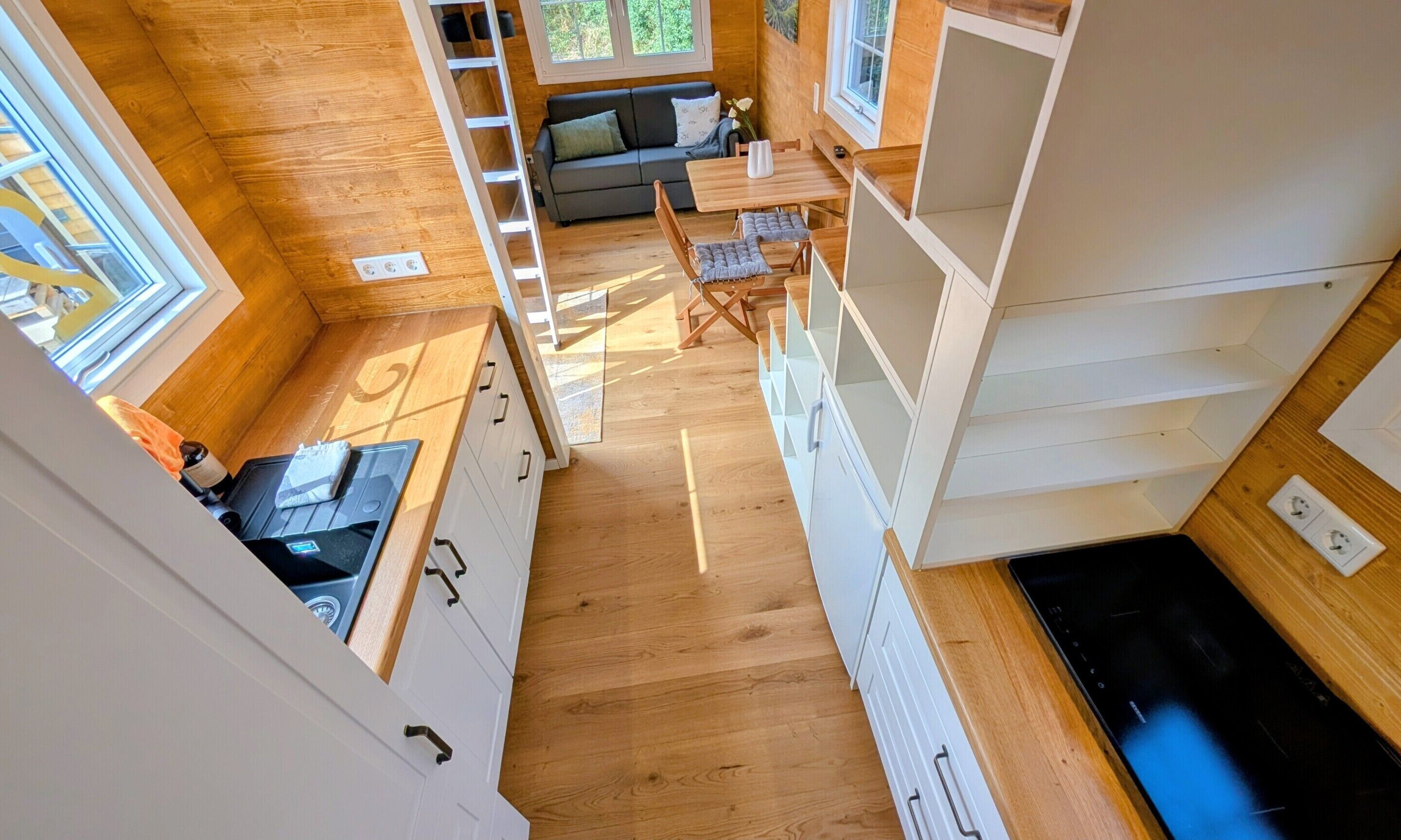 Een kleine keuken met houten kastjes, een eethoek met een tafel en stoelen, en een ingebouwde bank in de woonruimte.
