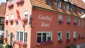 Un edificio con el nombre "Gasthof Rose" en su fachada, con varias ventanas adornadas con macetas de flores y un techo de tejas tradicional.